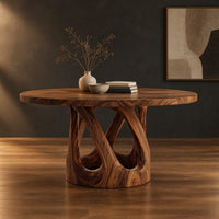 Round dining table on a pedestal of crossing curved struts in a dark studio against a charcoal plaster wall