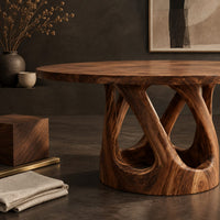 Corner detail of round dining table on a pedestal of crossing curved struts beside wood, brass and linen samples