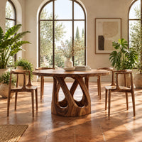 Round dining table on a pedestal of crossing curved struts in a bright dining room with arched windows and plants