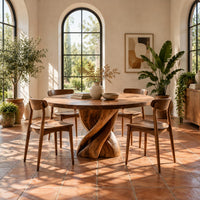 Round dining table with a twisted ribbon pedestal in a bright dining room with arched windows and plants