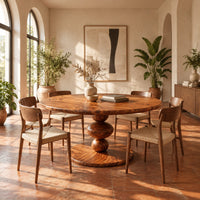 Round dining table with a pedestal of three stacked orbs in a bright dining room with arched windows and plants