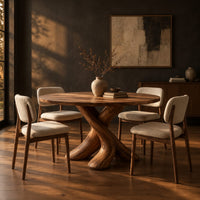 Circular dining table with two crossed branch shaped legs and wide curved feet in a dark dining room at golden hour