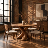 Circular dining table with two crossed branch shaped legs and wide curved feet in an industrial loft dining room with exposed brick