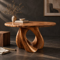 Corner detail of circular dining table on a sculpted pedestal with a large open loop beside wood, brass and linen samples
