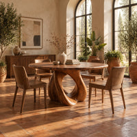 Circular dining table on a sculpted pedestal with a large open loop in a bright dining room with arched windows and plants