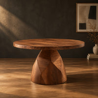 Circular dining table with a faceted bell shaped pedestal base in a dark studio against a charcoal plaster wall