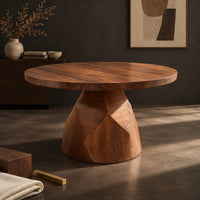 Corner detail of circular dining table with a faceted bell shaped pedestal base beside wood, brass and linen samples