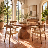 Circular dining table with a faceted bell shaped pedestal base in a bright dining room with arched windows and plants