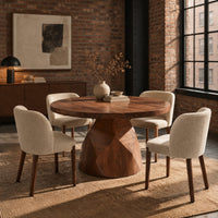 Circular dining table with a faceted bell shaped pedestal base in an industrial loft dining room with exposed brick