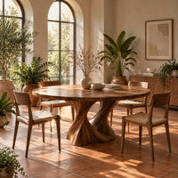 Round dining table on a twisted pedestal base in a bright dining room with arched windows and plants