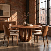 Round dining table on a pedestal made of arched wood columns in an industrial loft dining room with exposed brick
