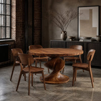 Round dining table with a spiral twist pedestal base and a wide flat foot in an industrial loft dining room with exposed brick