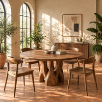 Circular dining table on branching arched pedestal legs in a bright dining room with arched windows and plants