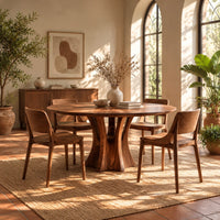 Round dining table with a flared pedestal base and a radiating grain top in a bright dining room with arched windows and plants