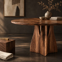 Corner detail of round dining table with a flared sculpted pedestal base beside wood, brass and linen samples