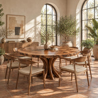 Circular dining table with a swirl grain top and flared trunk shaped legs in a bright dining room with arched windows and plants