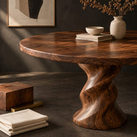 Corner detail of round wooden dining table on a twisted pedestal base beside wood, brass and linen samples