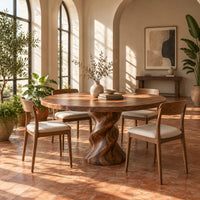 Round wooden dining table on a twisted pedestal base in a bright dining room with arched windows and plants