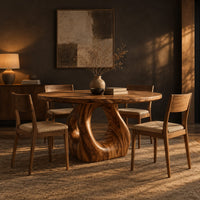 Circular wooden dining table on a sculpted pedestal with an open oval center in a dark dining room at golden hour