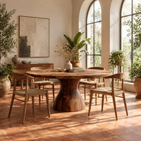 Round dining table with an hourglass pedestal base in a bright dining room with arched windows and plants
