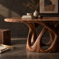 Corner detail of round dining table on an open base of interlaced curves beside wood, brass and linen samples