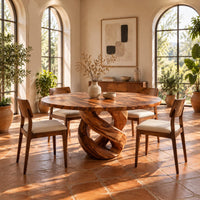 Round dining table with a twisted loop pedestal base in a bright dining room with arched windows and plants