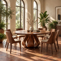 Round dining table on a petal shaped pedestal with a low disc foot in a bright dining room with arched windows and plants