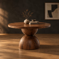 Round dining table with a radiating grain top and a sculpted hourglass base in a dark studio against a charcoal plaster wall