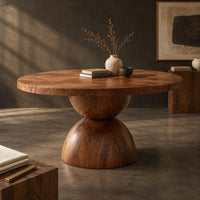 Corner detail of round dining table with a radiating grain top and a sculpted hourglass base beside wood, brass and linen samples