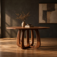 Round dining table with a thick pedestal base of arched wooden loops in a dark studio against a charcoal plaster wall