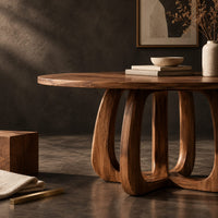 Corner detail of round dining table with a thick pedestal base of arched wooden loops beside wood, brass and linen samples