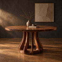 Round dining table with a flared pedestal base cut with tall arched openings in a dark studio against a charcoal plaster wall