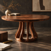 Corner detail of round dining table with a flared pedestal base cut with tall arched openings beside wood, brass and linen samples