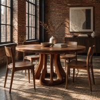 Round dining table with a flared pedestal base cut with tall arched openings in an industrial loft dining room with exposed brick