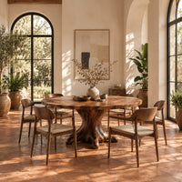 Circular dining table with a root shaped pedestal base in a bright dining room with arched windows and plants