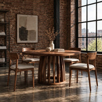 Circular dining table with a slatted drum pedestal base in an industrial loft dining room with exposed brick