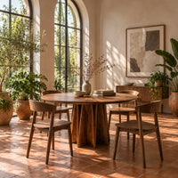 Round dining table with a sunburst grain top and a faceted star pedestal in a bright dining room with arched windows and plants