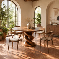 Round dining table with a twisted spiral pedestal and a flat disc foot in a bright dining room with arched windows and plants