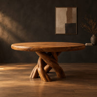 Round dining table with a twisted branch pedestal base in a dark studio against a charcoal plaster wall