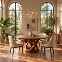 Round dining table with a twisted loop pedestal base in a bright dining room with arched windows and plants