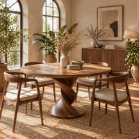 Round dining table with a twisted pedestal and disc base in a bright dining room with arched windows and plants