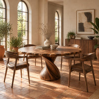 Circular dining table with twisted pedestal base and rippled edge in a bright dining room with arched windows and plants