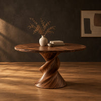 Round dining table with a twisted sculpted pedestal base in a dark studio against a charcoal plaster wall