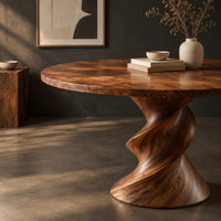 Corner detail of round dining table with a twisted sculpted pedestal base beside wood, brass and linen samples