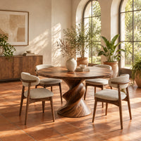 Round dining table with a twisted sculpted pedestal base in a bright dining room with arched windows and plants