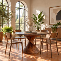 Round dining table on a twisted spiral pedestal in a bright dining room with arched windows and plants