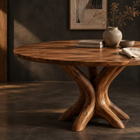 Corner detail of circular dining table with a pedestal of twisting branch shaped limbs beside wood, brass and linen samples