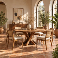 Circular dining table with a pedestal of twisting branch shaped limbs in a bright dining room with arched windows and plants