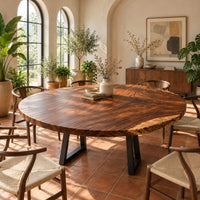 Circular wood table top with swirling grain and one natural edge in a bright dining room with arched windows and plants