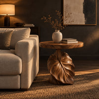 Round side table on a pedestal carved like a large leaf in a dark living room at golden hour